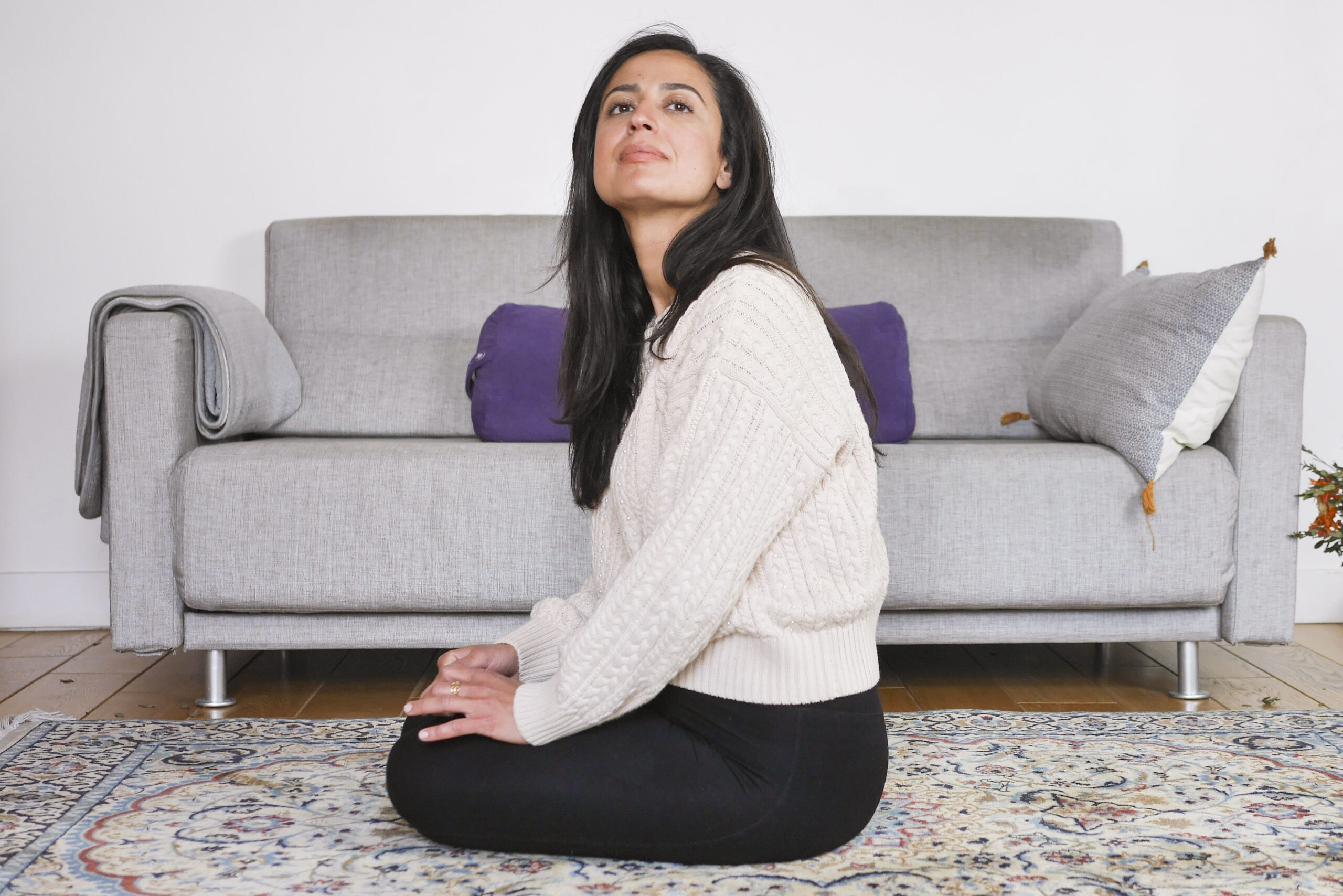 Femme assise chez elle, attentive à son environnement, évoquant une difficulté à se relâcher